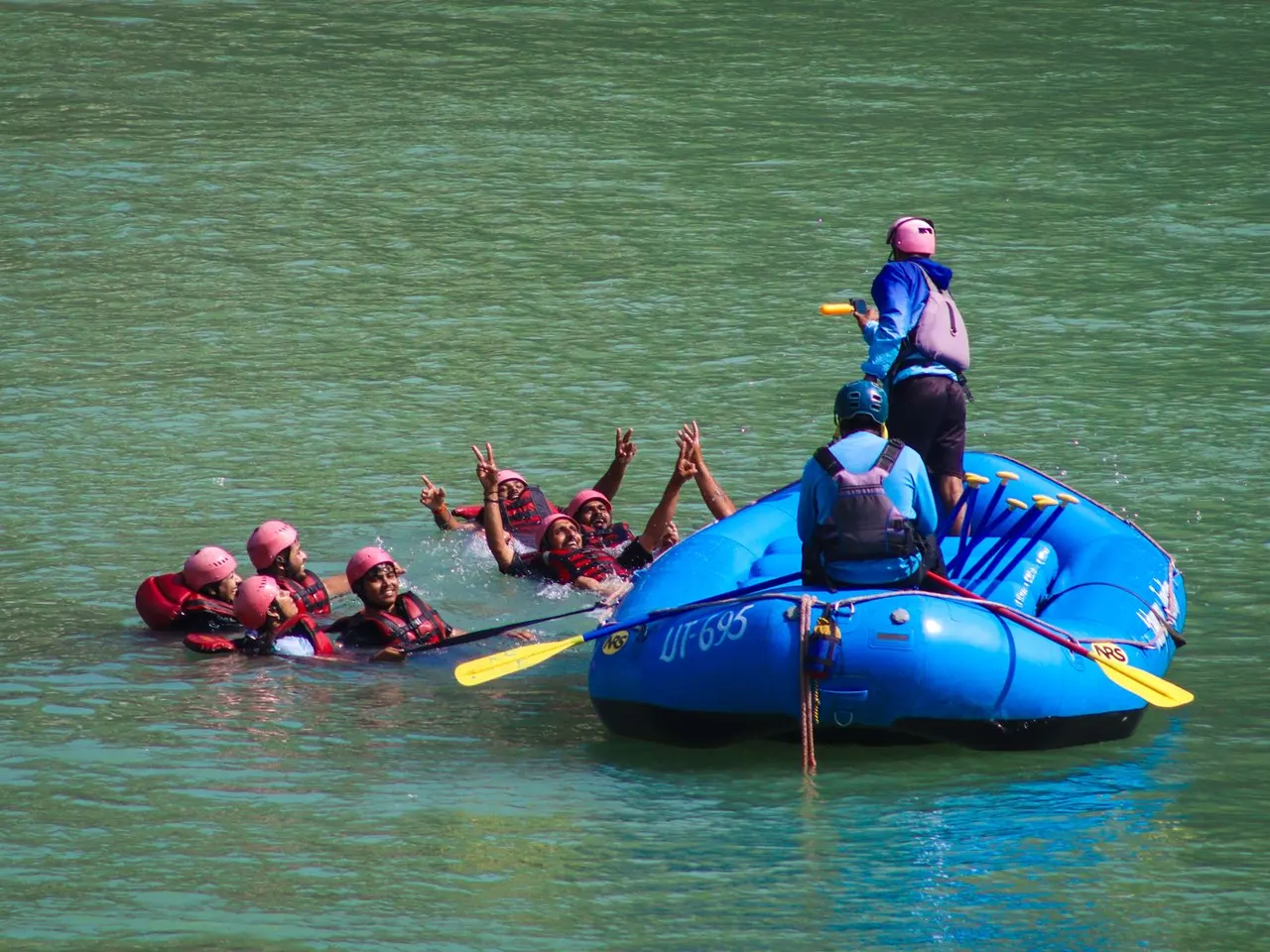 Rafting participants practising a water-rescue drill beside a blue raft