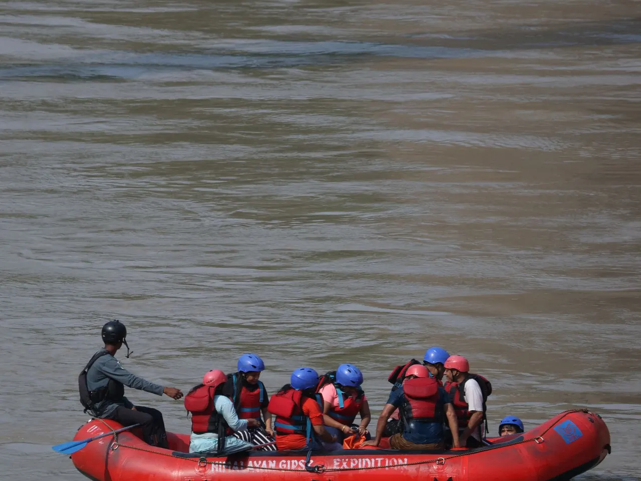 Guide steering a red raft with a helmeted group on calm water