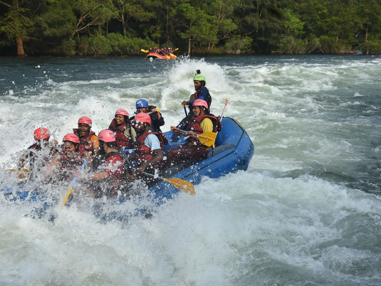 Helmeted rafting group paddling through a breaking whitewater wave