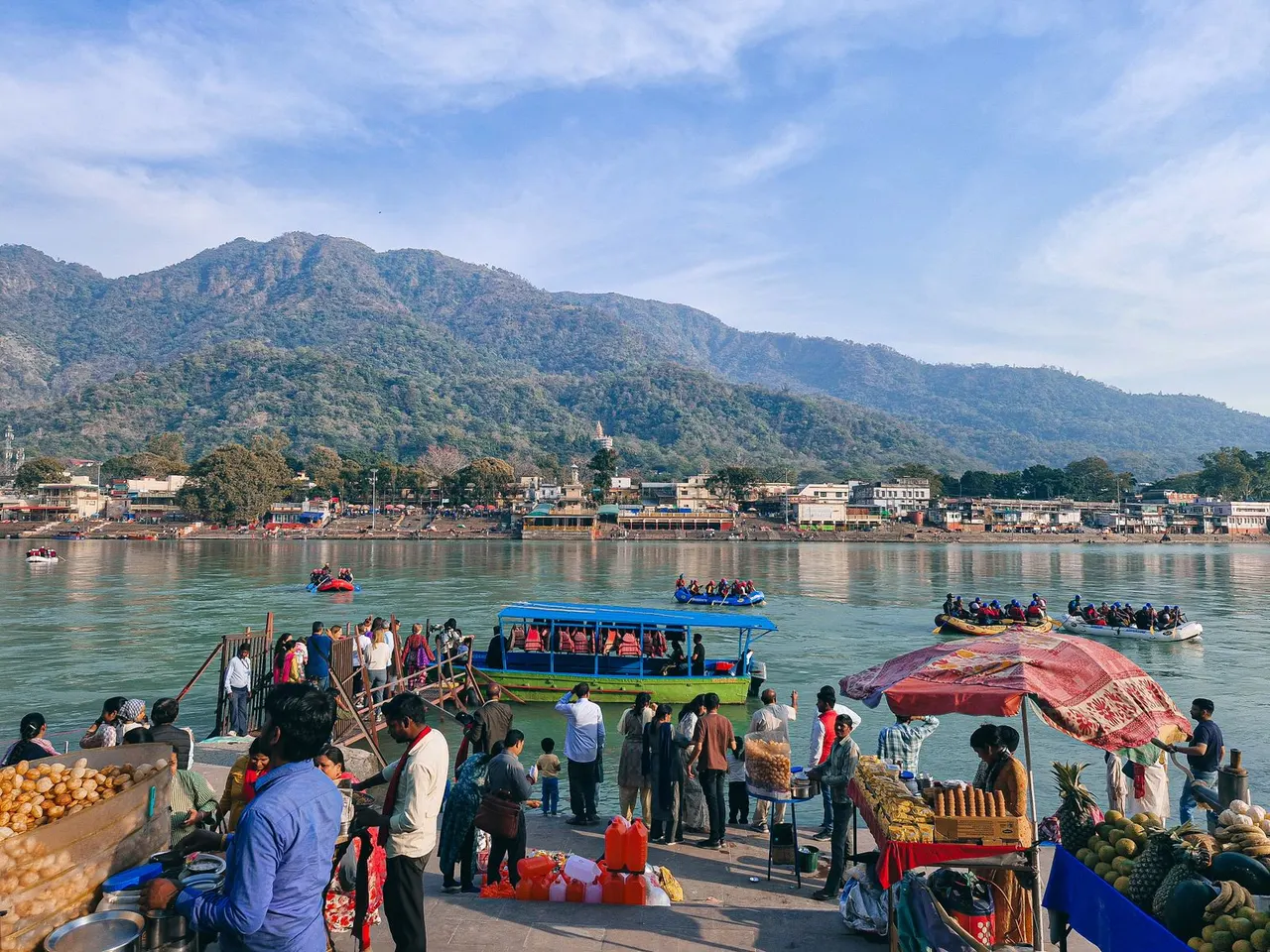 Busy Rishikesh riverfront with boats, visitors and green hills
