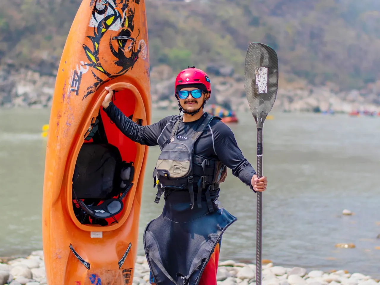 Whitewater kayaker carrying an orange kayak on a rocky riverbank