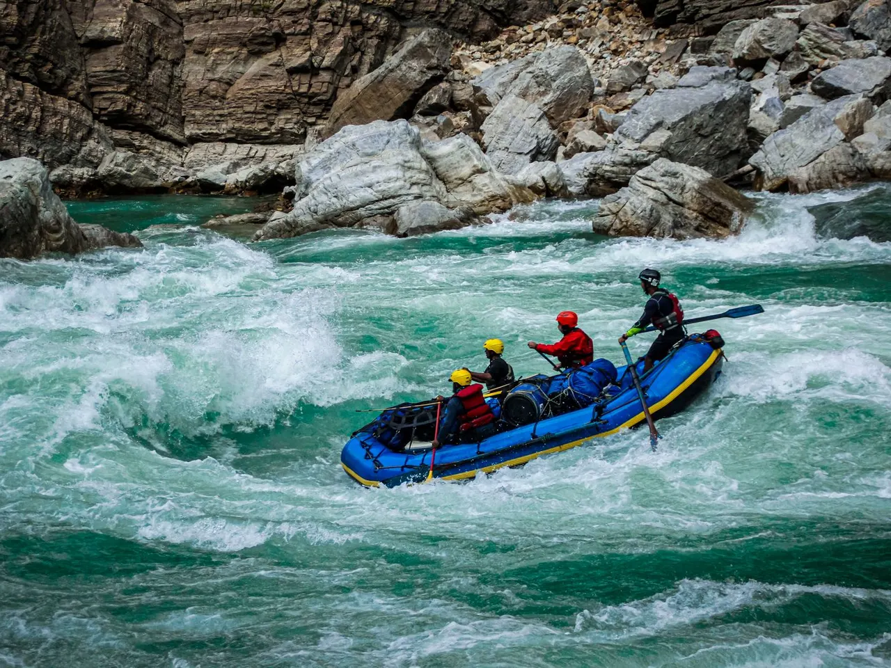 Blue raft carrying a group through whitewater beside rocky banks
